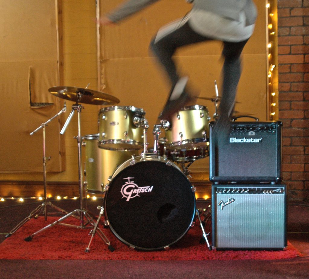 A person is jumping in front of a drum. 